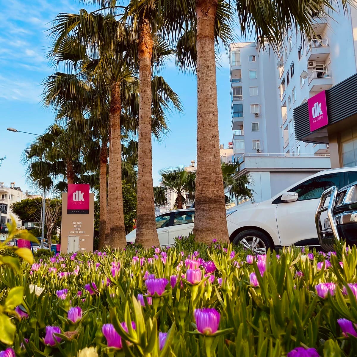 The DK Klinik sign among palm trees and flowers outside the clinic in Antalya