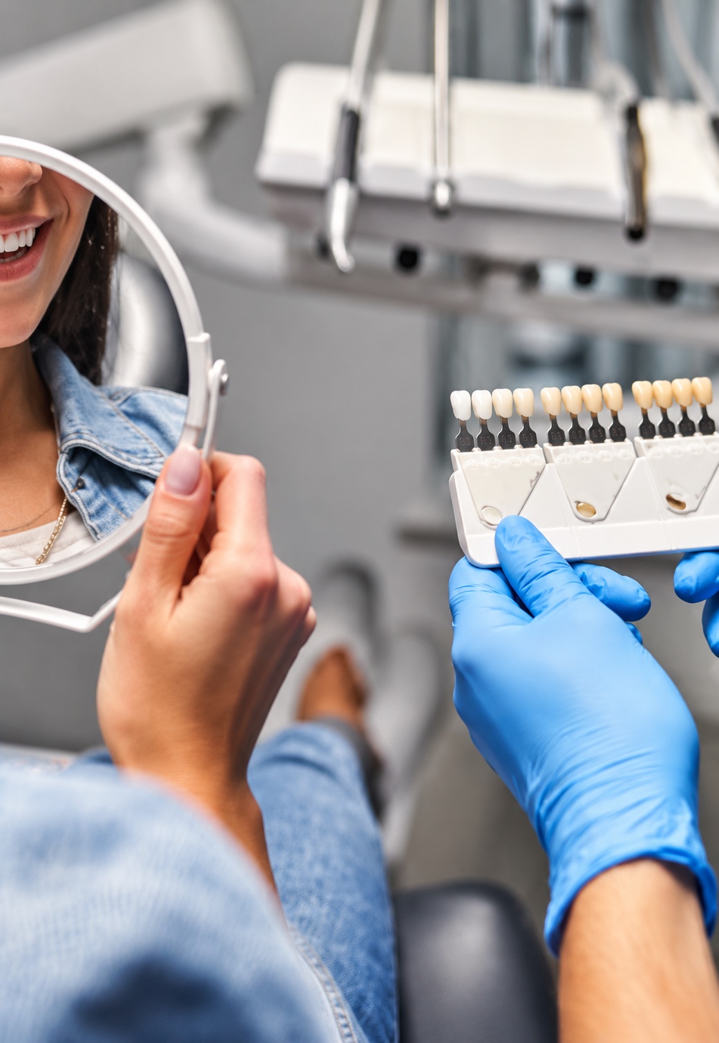 Dental patient checking her smile in a mirror while a dentist holds a shade guide